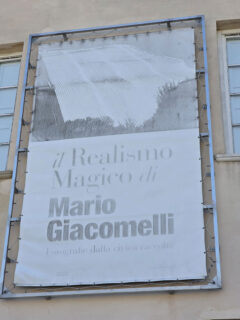 Il tabellone, ormai scolorito, esposto sulla facciata di Piazza del Duca che pubblicizza la mostra di Mario Giacomelli